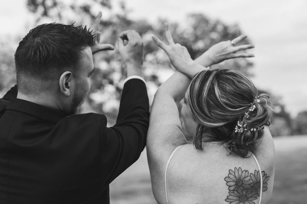 Bride and groom spelling 'LOVE' with hand signs from behind in black and white