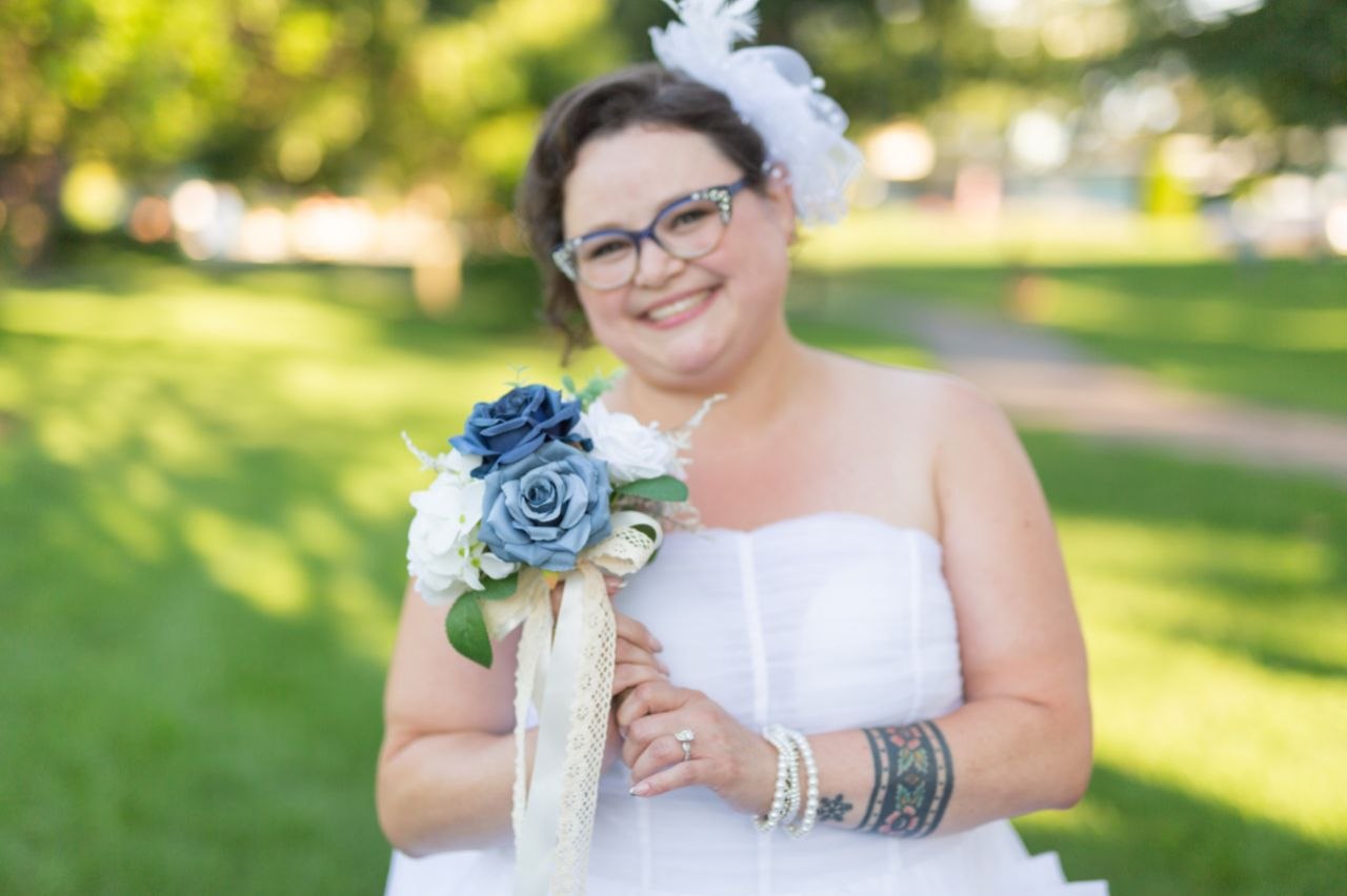 Bride holding bouquet of blue and white flowers, smiling in sunlight