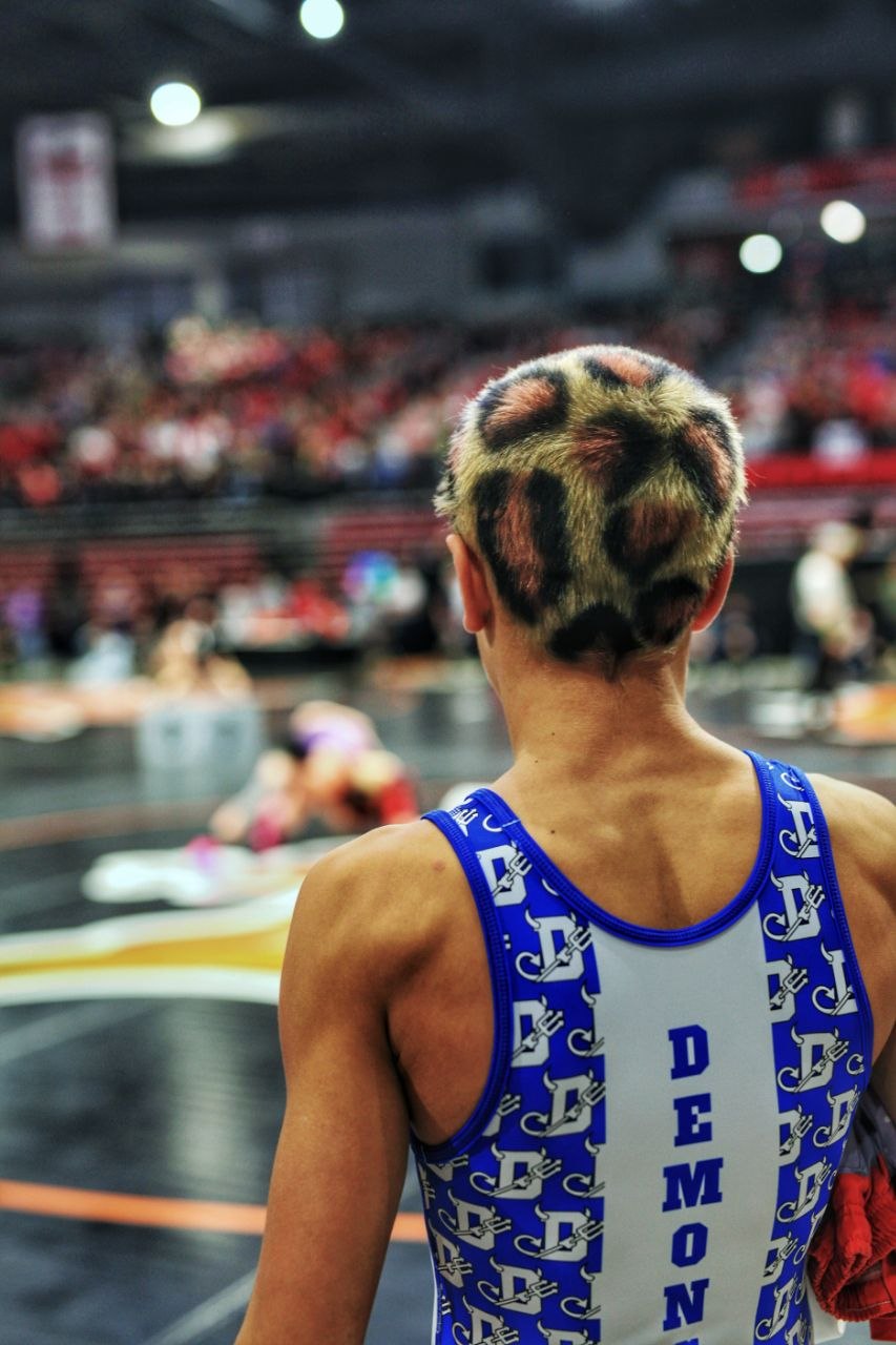 Wrestler with leopard-print buzzcut and DEMON singlet standing on mat